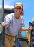 Female farm worker steps out of yellow tractor while smiling.